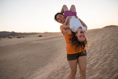 Mother holding her smiling daughter upside down on sand duneの写真素材