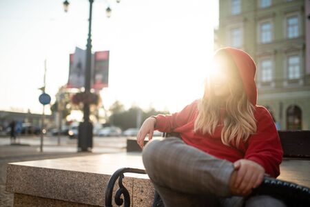 Woman sitting with legs crossed on bench, flare backgroundの写真素材