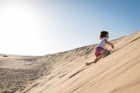 Courageous little girl climbing sand dune under the blue skyの写真素材