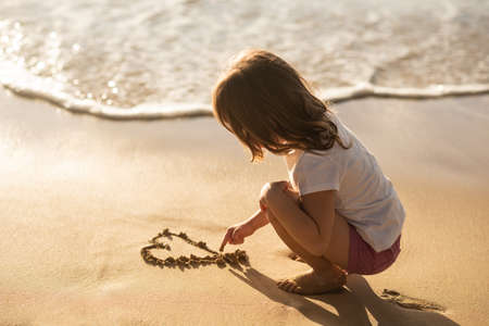 Kid making sand heart on the beachの写真素材