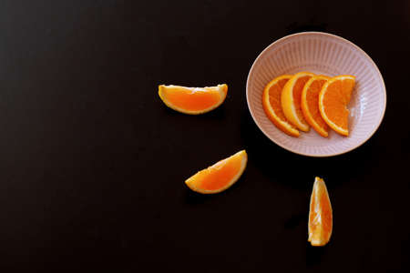 Fresh orange for breakfast with a black background. the fruit is in little slices in a pink plates.の写真素材