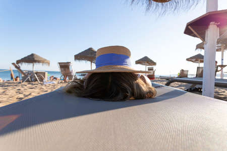 Rear View of a beautiful Asian woman playing with a summer sombrero on the beach at sunset wearing a...