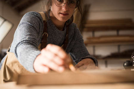 A young couple of carpenter working together in a small wood laboratory using a drill machine for timber. Couple crafting new home furniture in a carpentry workshop. young entrepreneurs concept A young couple of carpenter working together in a small wood laboratory using a drill machine for timber. Couple crafting new home furniture in a carpentry workshop. young entrepreneurs concept