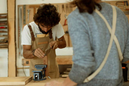 A young couple of carpenter working together in a small wood laboratory using a drill machine for timber. Couple crafting new home furniture in a carpentry workshop. young entrepreneurs conceptの写真素材