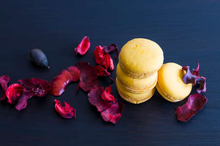 Close-up of breakfast morning with yellow macaroons lemon taste. close-up of french dessert on the black background and flowers around in a simple vintage composition. Food photography.の写真素材