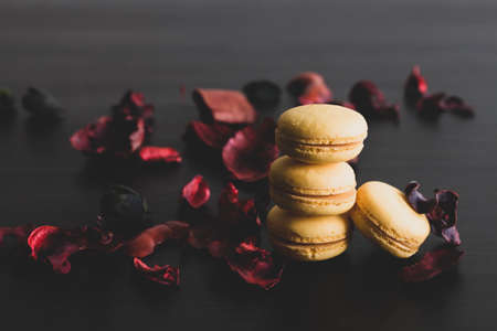 Close-up of breakfast morning with yellow macaroons lemon taste. close-up of french dessert on the black background and flowers around in a simple vintage composition. Food photography.の写真素材