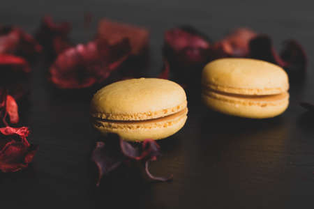 Close-up of breakfast morning with yellow macaroons lemon taste. close-up of french dessert on the black background and flowers around in a simple vintage composition. Food photography.の写真素材