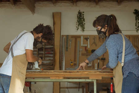 Young couple of carpenter working and crafting with wood in a workshop building furniture for interior design. Young couple entrepreneurs running a small business in a carpentry. Business people.の写真素材