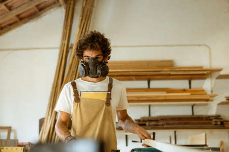 A young man working as carpenter in his wood workshop. Wood worker designing and handcrafting new...