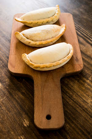 Traditional baked Argentine empanadas savory pastries with meat beef stuffing or vegetables against wooden background and spicy sauce. Latin American fried food.の写真素材