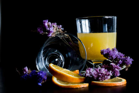 Glass of healthy Orange juice with pulp and sliced fruits isolate on black background with purple flowers. Orange juice and fresh fruits on table.の写真素材