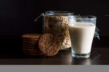 Serving healthy morning breakfast with corn flakes Whole grains muesli, fresh milk in a glass and Pile of Delicious Chocolate homemade Chip Cookies on a vintage dark background. Aesthetic compositionの写真素材