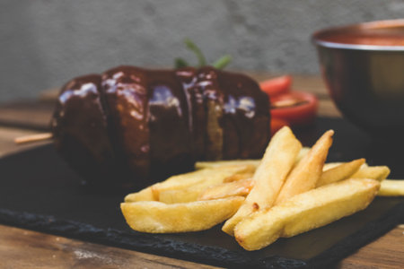 a mix of american fast food, junkie food. A fried meat like hamburger or beef steak with different sauces of ketchup and mayo with crunchy french fries, healthy tomato salad and a fresh mint beverage.の写真素材