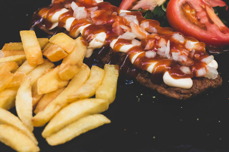 American fast food. A couple of beef and chicken skewers with a delicious peanuts sauce with some fresh salad with tomatoes and crunchy french fries. Delicious meat steaks on a wooden background.の写真素材