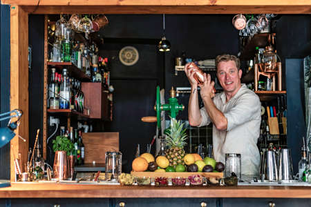 View of a cheerful man working as bartender in a colorful cocktail bar, view of a professional barman shaking a drink behind the counter, Lisbon, Portugal.の写真素材
