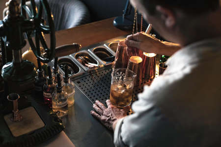 An expert bartender mixing a cocktail in a glass mixer with a long spoon, standing behind the counter of his beautiful cocktail bar in a night club.の写真素材