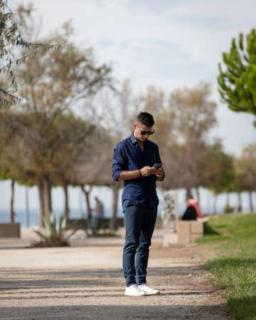 Beautiful and attractive young middle aged man walking alone and using the smart phone along the...