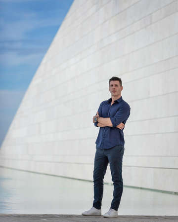 Portrait of a beautiful young man posing for a photo session along the tejo riverside in Lisbon, Portugal. Stylish freelance architect relaxing alone near the urban concept building in downtown.の写真素材