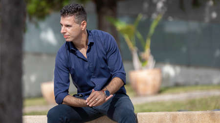Portrait of a young classy entrepreneur relaxing alone along the Lisbon riverside in Portugal. Classy business man wearing a blue elegant shirt and formal outfit. Successful lifestyle concept.の写真素材