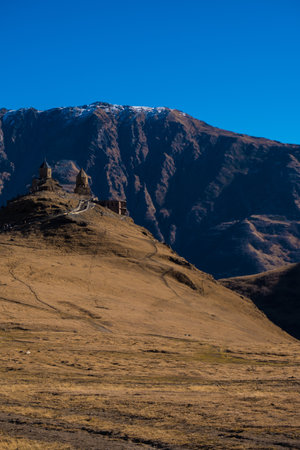 Kazbegi, Georgia : 10-11-2022 : amazing panorama of ancient Gergeti Trinity Church and glorious Caucasus mountains, Panoramic landscape of beautiful natural mountains  peaks and meadow, Kazbegi, Georgiaの写真素材
