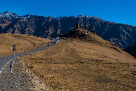 Kazbegi, Georgia : 10-11-2022 : amazing panorama of ancient Gergeti Trinity Church and glorious Caucasus mountains, Panoramic landscape of beautiful natural mountains  peaks and meadow, Kazbegi, Georgiaの写真素材