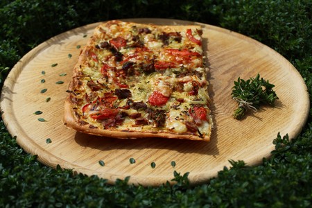 a piece of pizza on a wooden board in a thyme fieldの写真素材