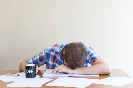 Young adult asleep over books holding a cup 