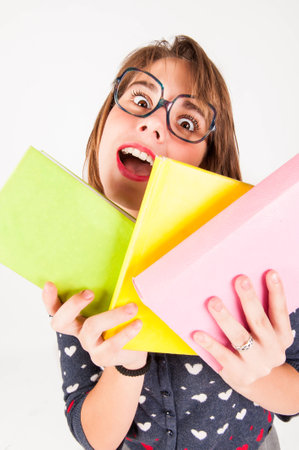 Cute nerdy girl holding books whilst looking at camera  Studio shot の写真素材