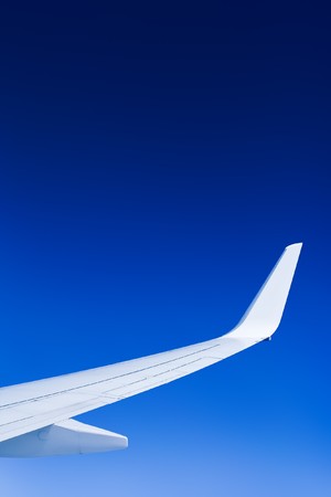 A bright airplane wing against a perfect blue sky.の写真素材