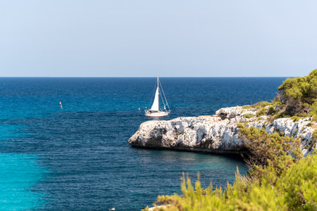 At Cala Llombards in Mallorca, Spain, the tranquil waters of the Mediterranean meet a pristine white sandy beach, with boats gently bobbing on the horizonの写真素材