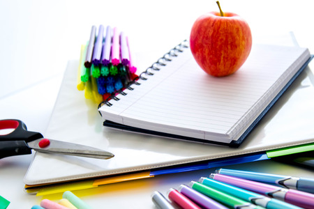 bright colored back to school supplies and an apple for the teacher