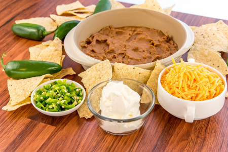 preparation of layered bean dip with jalapenos, sour cream and cheddar cheeseの写真素材