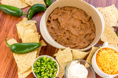 preparation of layered bean dip with jalapenos, sour cream and cheddar cheeseの写真素材