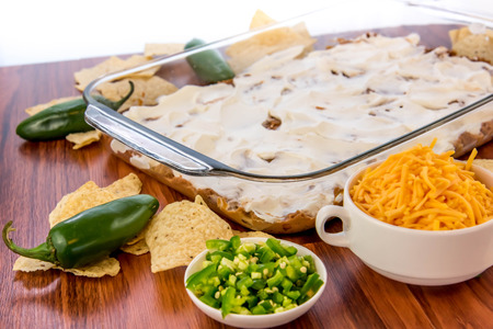 preparation of layered bean dip with jalapenos, sour cream and cheddar cheeseの写真素材