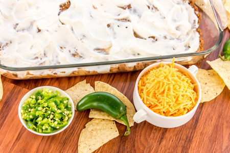 preparation of layered bean dip with jalapenos, sour cream and cheddar cheeseの写真素材