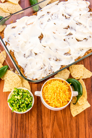 preparation of layered bean dip with jalapenos, sour cream and cheddar cheeseの写真素材
