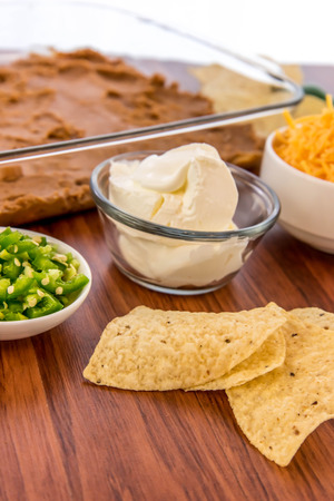 preparation of layered bean dip with jalapenos, sour cream and cheddar cheeseの写真素材