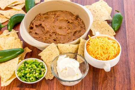 preparation of layered bean dip with jalapenos, sour cream and cheddar cheeseの写真素材