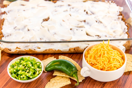 preparation of layered bean dip with jalapenos, sour cream and cheddar cheeseの写真素材