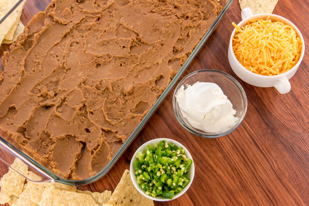 preparation of layered bean dip with jalapenos, sour cream and cheddar cheeseの写真素材