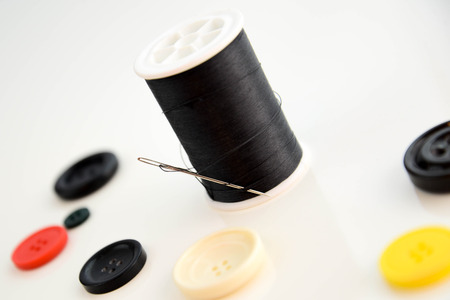 threaded needle, black thread spool and red, black, white, and yellow buttonsの写真素材