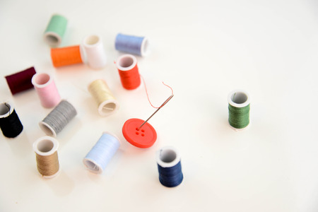 red thread through needle eye and red button with multi colored thread spoolsの写真素材