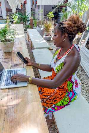 afro woman working with laptop outdoors, in a garden, a terrace of a cafe, outdoors, with casual clothesの写真素材