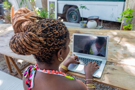 afro woman working with laptop outdoors, in a garden, a terrace of a cafe, outdoors, with casual clothesの写真素材