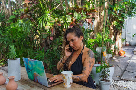 latin woman working on laptop, video conference, celebrating achievements online, outdoorsの写真素材