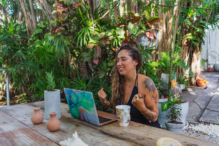 latin woman working on laptop, video conference, celebrating achievements online, outdoorsの写真素材