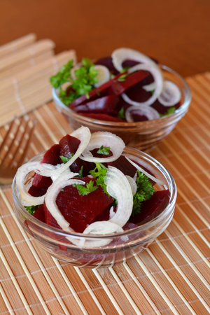 Fresh sliced beetroot salad with onion and parsley on a glass bowl on a tableの写真素材