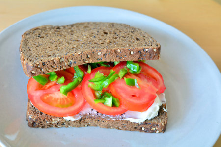 Healthy wholemeal sandwich with sliced tomatoes and vegetables on a plateの写真素材