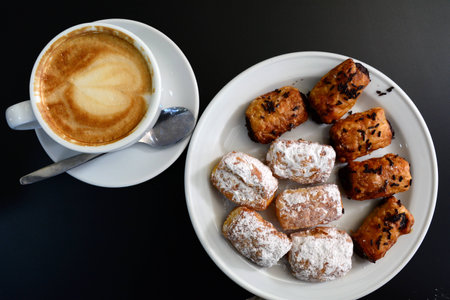 Cup of delicious foamy cappuccino with dessert on a black background.