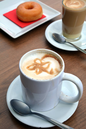Delicious foamy cappuccino on a white cup and donut on a plate.の写真素材